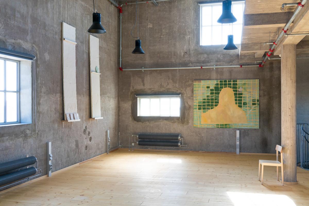 Artworks in a high space with concrete walls.